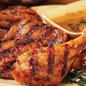 Grilled chicken drumsticks with bold char marks served with dipping sauce and herbs