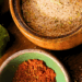 Overhead view of chili lime salt in a wooden salt cellar with limes, chili powder, and spilled seasoning on a wooden board