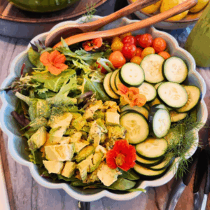 Overhead view of a spring salad in a scalloped bowl, topped with cucumbers, cherry tomatoes, avocado, edible nasturtiums, and fresh dill