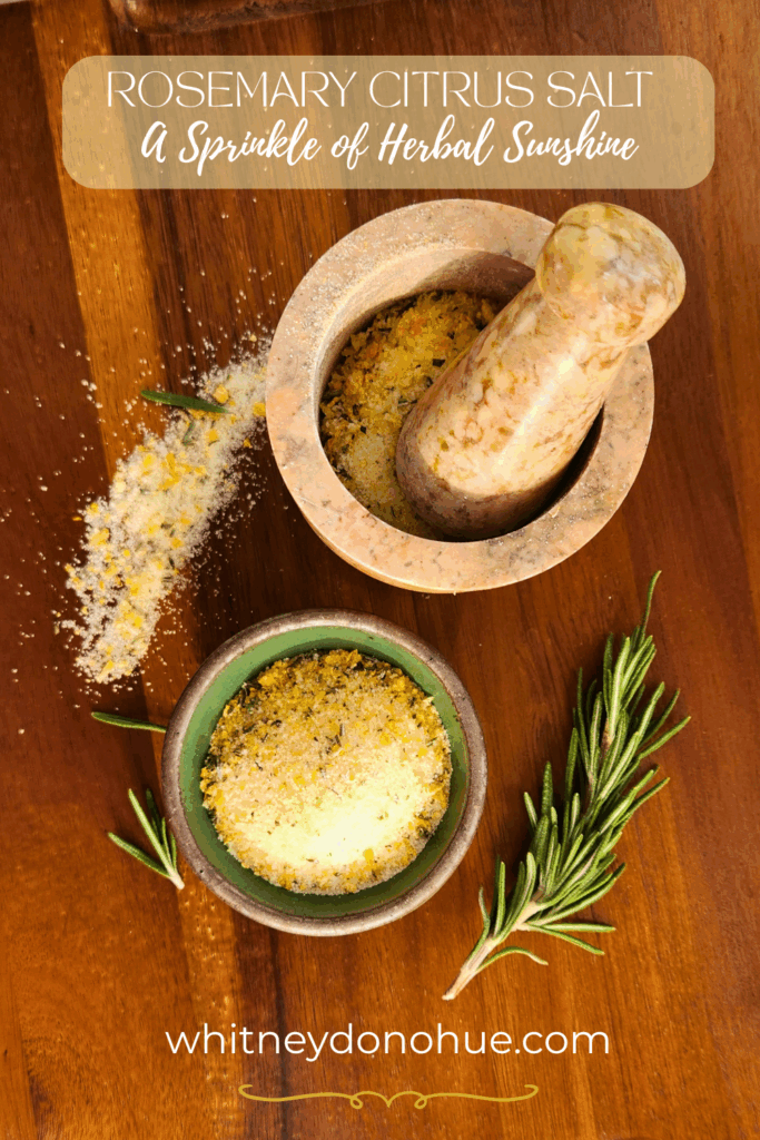 Overhead view of homemade rosemary citrus salt in a green bowl and marble mortar, with fresh rosemary sprigs and scattered salt on a wooden board.