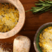 Overhead view of rosemary citrus salt in a marble mortar and ceramic bowl with a fresh rosemary sprig on a wooden board.