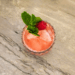 Coral pink Wild May Cup mocktail garnished with mint and a fresh raspberry in a pressed glass