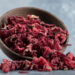 Dried hibiscus petals in a rustic wooden bowl on a neutral background