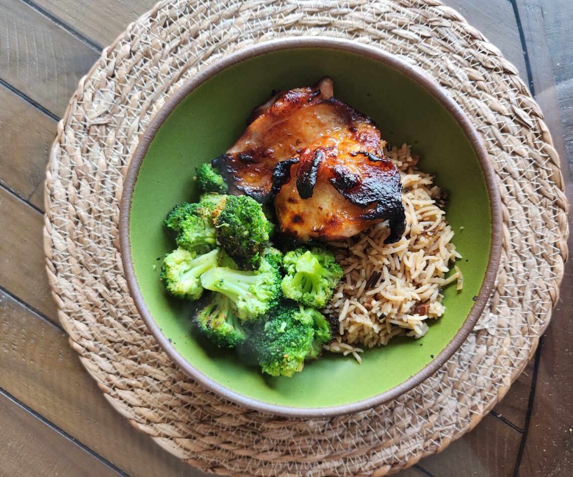 Grilled Chinese chicken thigh served with broccoli and wild rice pilaf in a green bowl.