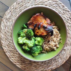 Overhead view of grilled Chinese chicken, broccoli, and rice in a green bowl.