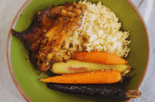 Grilled Cajun chicken thigh served with seasoned rice and colorful roasted carrots in a green bowl.