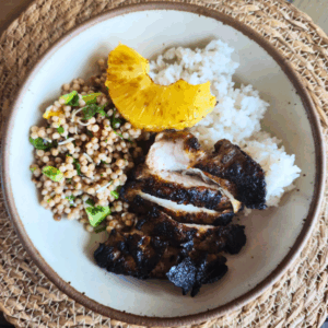 Sliced grilled Caribbean chicken served with coconut rice, chili-lime roasted pineapple, and a fresh Israeli couscous salad with corn and herbs on a ceramic plate.