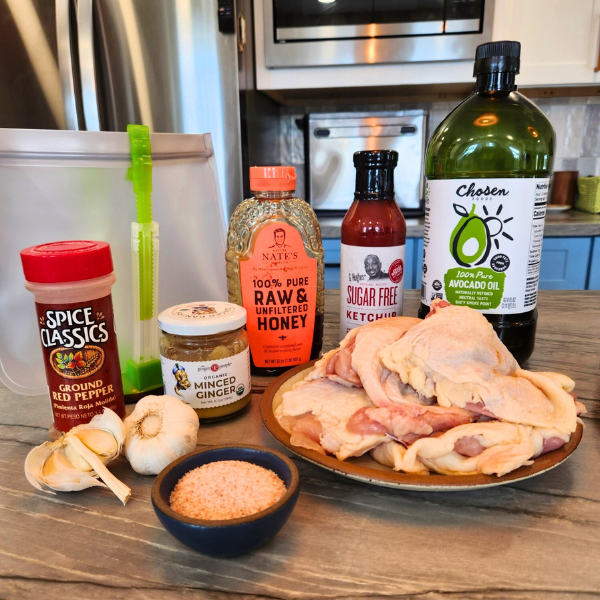 Ingredients for Chinese Chicken marinade including garlic, ginger, ketchup, honey, red pepper, and chicken thighs arranged on a kitchen counter