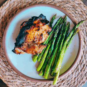 Grilled Thai chicken thigh served with roasted asparagus on a ceramic plate.