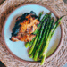 Grilled Thai chicken thigh served with roasted asparagus on a ceramic plate.