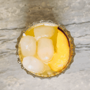 Top-down view of Peach Moon Elixir mocktail in a faceted glass with ice and a crescent peach slice