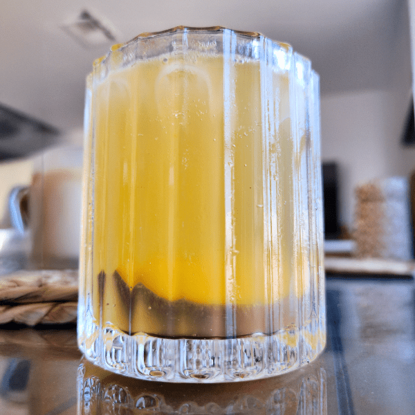 Side view of the Peach Moon Elixir mocktail in a faceted glass, with a crescent peach slice resting at the bottom, glowing through the golden drink