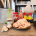 Ingredients for Thai Chicken marinade including soy sauce, honey, ground cumin, fresh garlic and ginger, arranged beside raw chicken thighs on a kitchen counter.