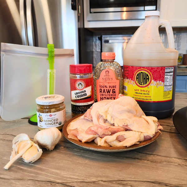 Ingredients for Thai Chicken marinade including soy sauce, honey, ground cumin, fresh garlic and ginger, arranged beside raw chicken thighs on a kitchen counter.
