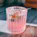 Pink floral mocktail in a crystal glass with a sugared lavender and rose petal rim, garnished with a lavender sprig, glowing in natural sunlight on a marble countertop.