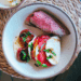 Sliced Santa Maria-style tri-tip on a cutting board, grilled medium-rare with visible sear marks. Fresh heirloom tomatoes and peaches are arranged beside the beef.